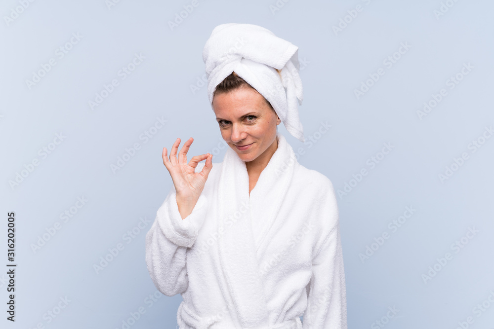 Woman in bathrobe over isolated blue background showing an ok sign with fingers Woman in bathrobe over isolated blue background showing an ok sign with fingers