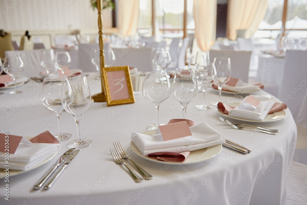 Table set with blank guest card, plate with pink and white serviette and cutlery on table, copy space. Place setting at wedding reception. Table served for wedding banquet in restaurant