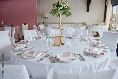 Table set with blank guest card, plate with pink and white serviette and cutlery on table, copy space. Place setting at wedding reception. Table served for wedding banquet in restaurant © mirage_studio