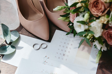 Luxury set of wedding invitations, wedding rings, elegant bride shoes on high heels on wood brown background. Honeymoon and wedding concept