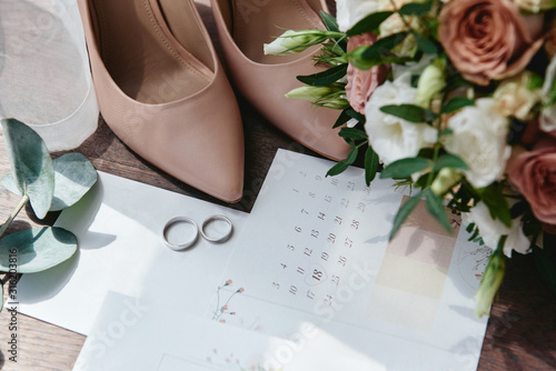 Luxury set of wedding invitations, wedding rings, elegant bride shoes on high heels on wood brown background. Honeymoon and wedding concept