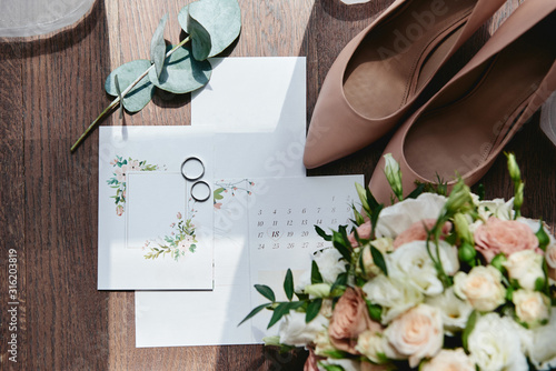 Luxury set of wedding invitations, wedding rings, elegant bride shoes on high heels on wood brown background. Honeymoon and wedding concept