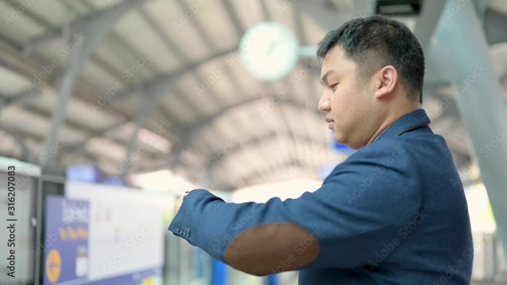 Asian businessman looking at his watch, waiting train platform Asian businessman looking at his watch, waiting train platform