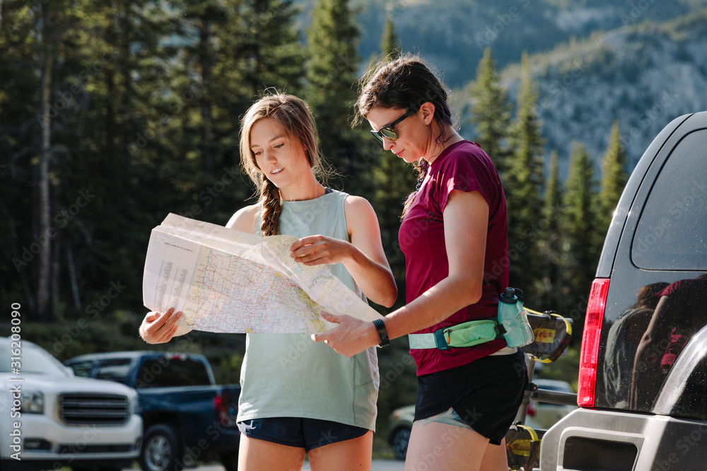 Female hikers looking at map in sunny parking lot Stock Photo | Adobe Stock