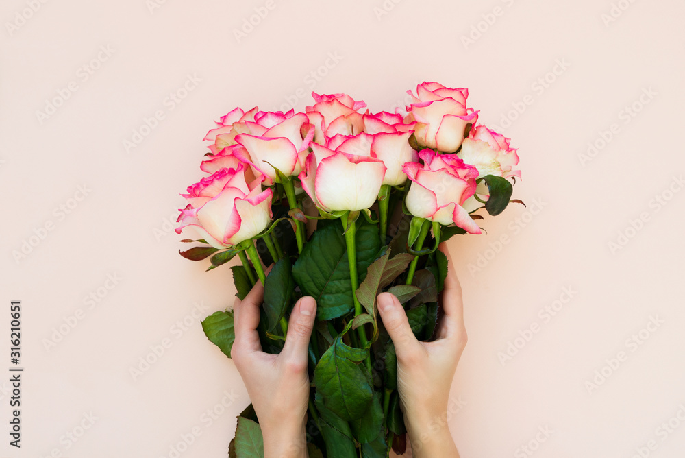 Hands holding bouquet of fresh pink roses wrapped pink ribbon on pink background. Top view. Flat lay. Copy space. Valentines day, mothers day or birthday celebration concept