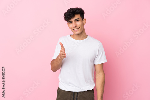 Young Argentinian man over isolated pink background handshaking after good deal