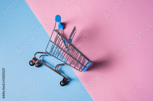 Empty miniature shopping cart on blue and pink color background.