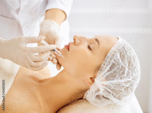 Beautiful woman receiving beauty injections with closed eyes. Beautician doctor hands doing beauty procedure to female face with syringe. Cosmetic medicine and surgery concept © rogerphoto