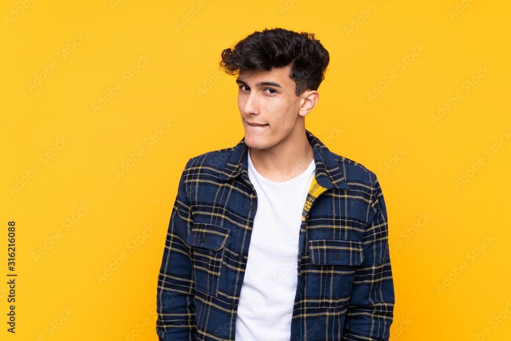 Young Argentinian man over isolated yellow background having doubts and with confuse face expression Young Argentinian man over isolated yellow background having doubts and with confuse face expression
