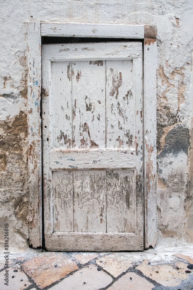 Old wooden door in a stone wall. Painted with white paint, cracks and damage on the textured surface.