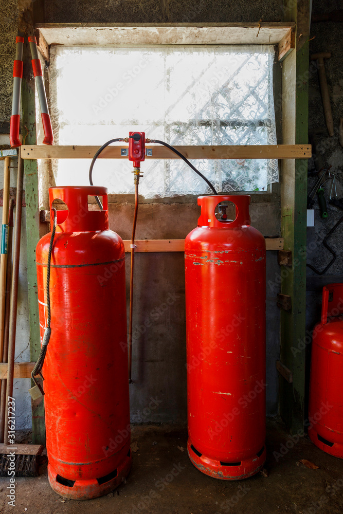 2 large red gas bottles infront of a window, in an old shed. 2 large red gas bottles infront of a window, in an old shed.