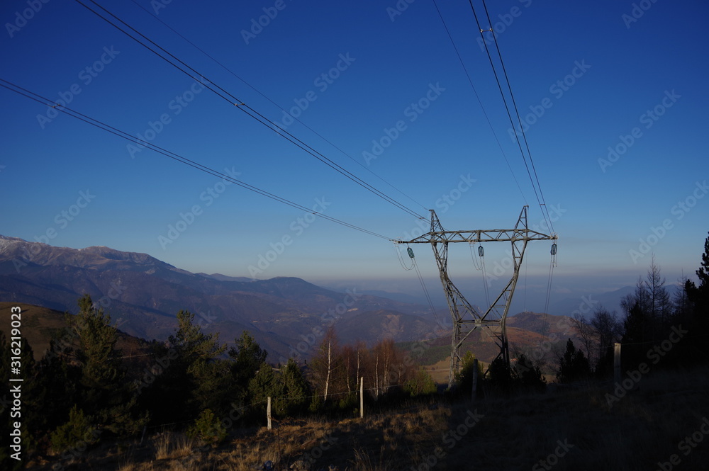 Ligne de haute tension électrique en montagne et soleil couchant