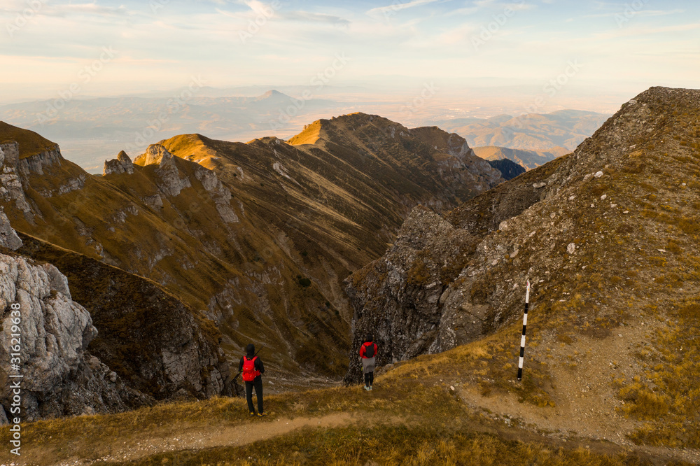 Aerial drone photograph with couple of hikers watching a beautiful sunset on top of Bucegi mountain ridge, during magical golden hour light in autumn season in Romania