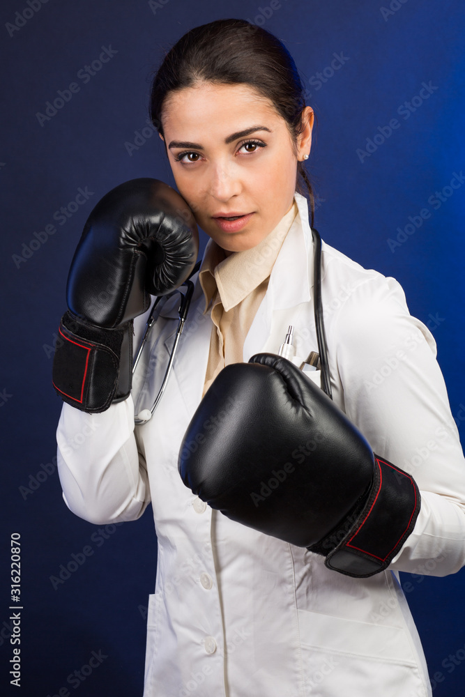 Medico donna in camice con i guantoni in mano fìdichiara guerra alle malattie - isolata su sfondo grigio Medico donna in camice con i guantoni in mano fìdichiara guerra alle malattie - isolata su sfondo grigio