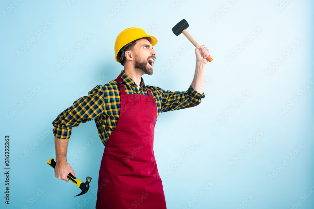 side view of angry workman holding hammers on blue side view of angry workman holding hammers on blue