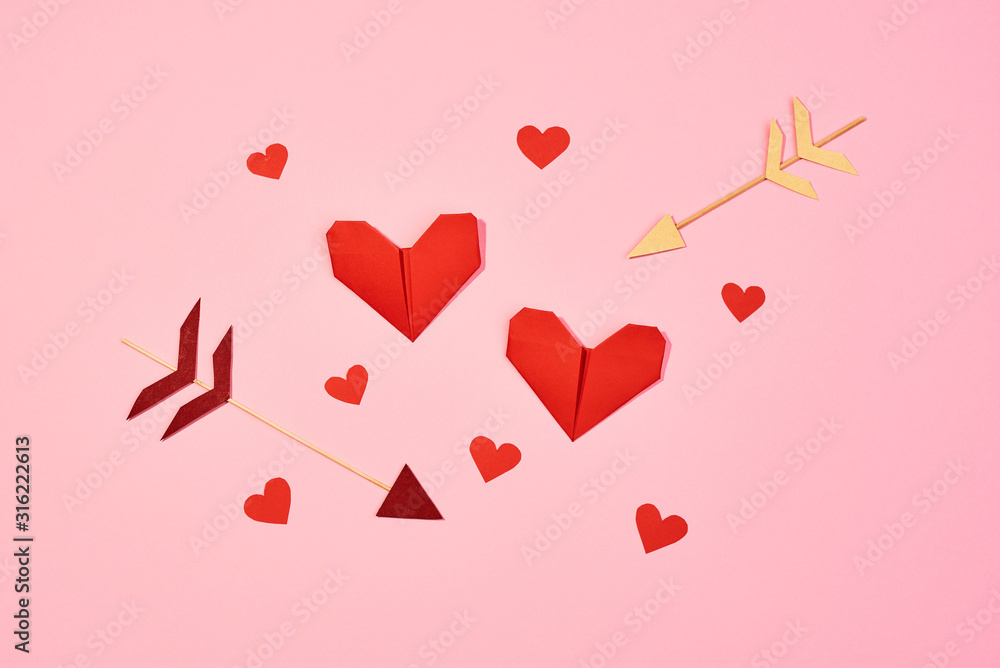 Valentine's Day. Red hearts made of paper and Cupid's arrows. Pink background. Top view.