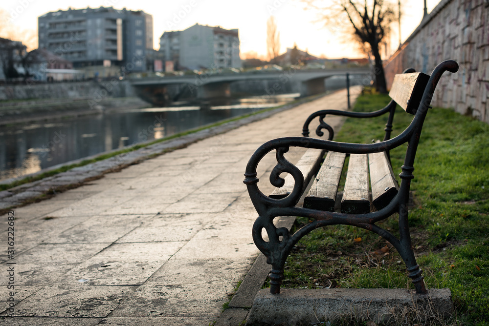 Bench at the promenade by the river bank in the autumn sunset and with soft focused background