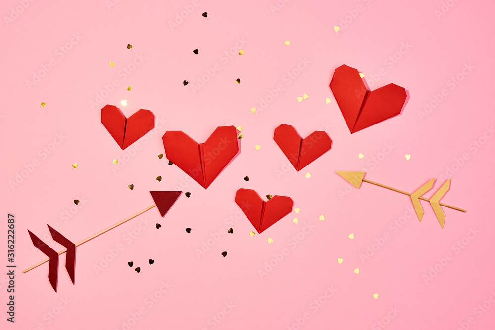 Valentine's day. Red paper hearts and Cupid's arrows isolated on pink.