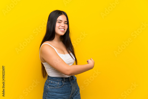 Young teenager Asian girl over isolated yellow background pointing back