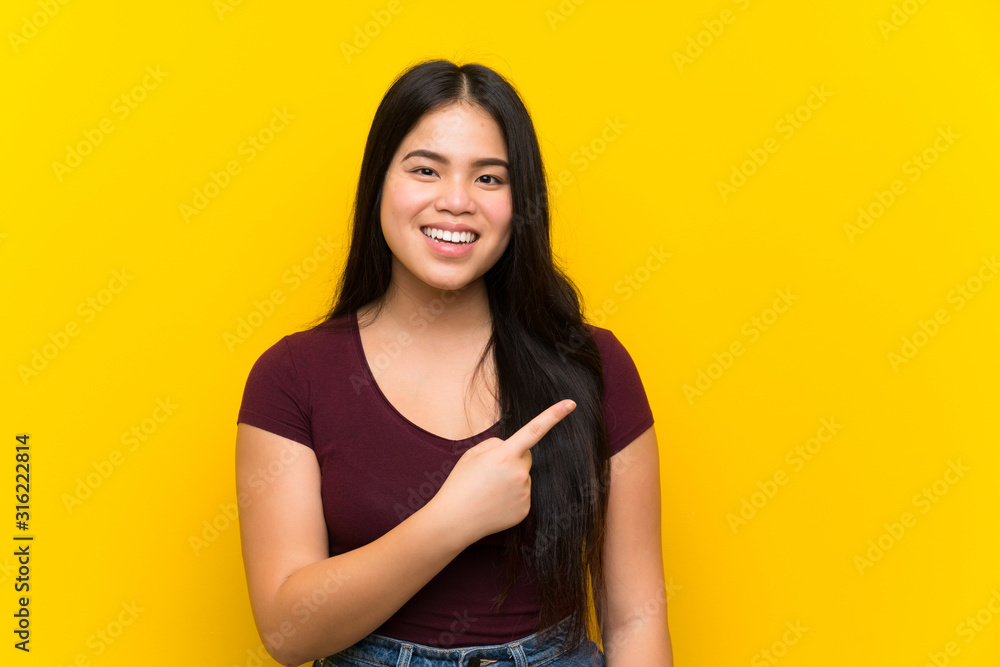Obraz premium Young teenager Asian girl over isolated yellow background pointing finger to the side