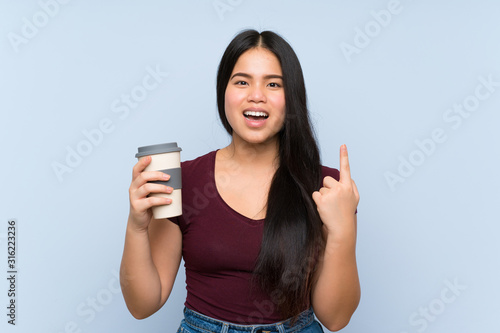 Young teenager Asian girl holding a take away coffee pointing up a great idea