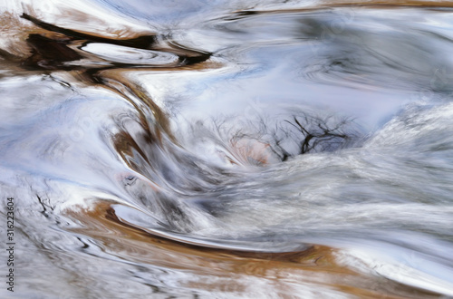 Rabbit River rapids captured with motion blur and with a reflection of bare trees in calm water, Michigan, USA