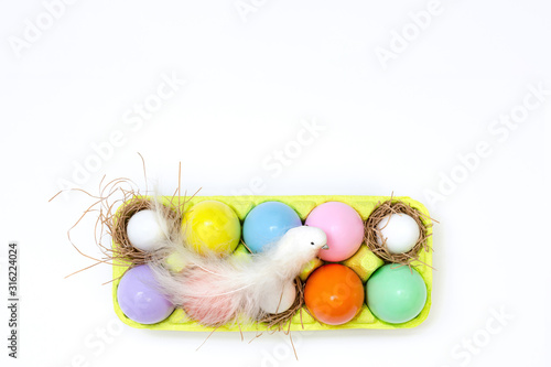 Top view of an Easter composition of painted eggs in bright juicy colors with a glossy texture that lie in the container and a white bird sits on top. Holiday concept, flat layout, easter, background