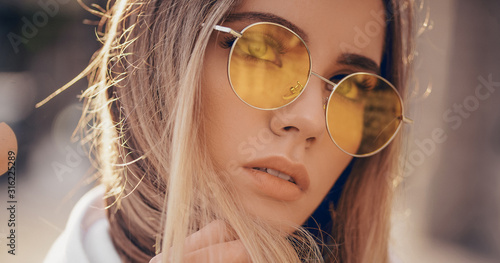 Portrait of beautiful stylish blonde woman in yellow sunglasses in outdoor.