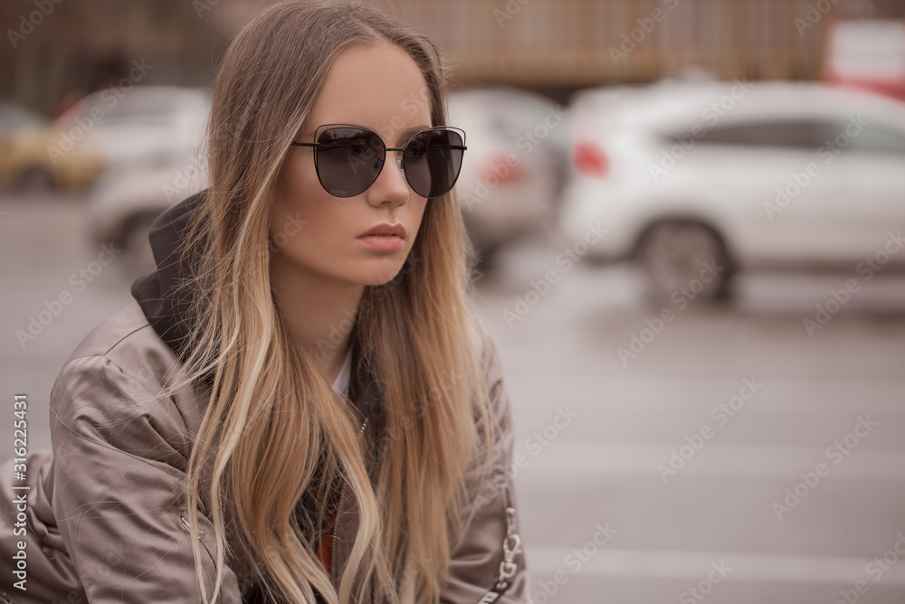 Stylish blonde woman in black sunglasses in outdoor.