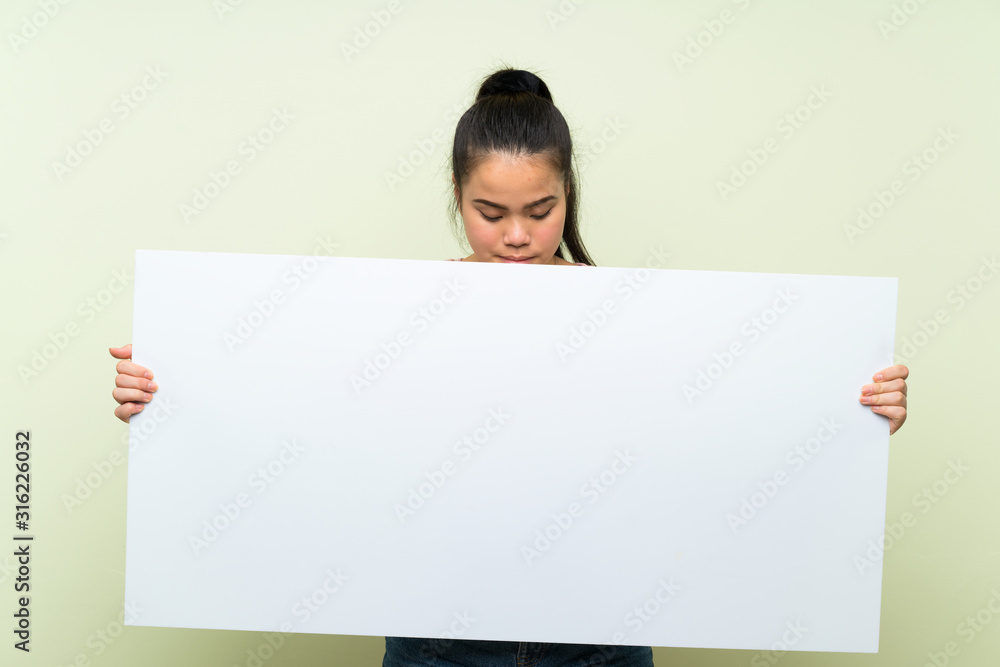 Young teenager Asian girl over isolated green background holding an empty white placard for insert a concept Young teenager Asian girl over isolated green background holding an empty white placard for insert a concept