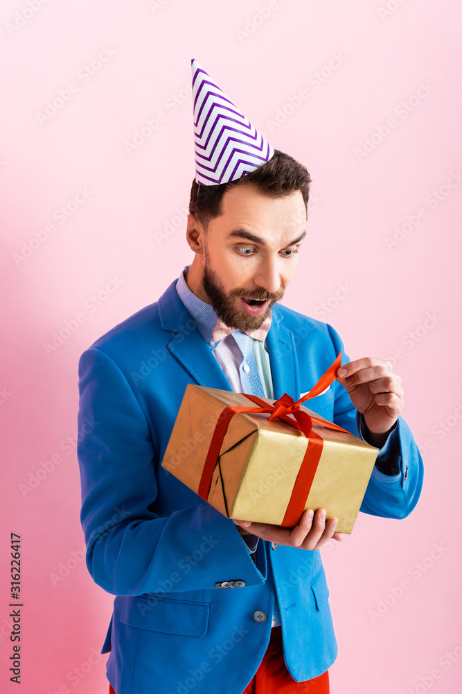 surprised businessman in suit looking at present on pink surprised businessman in suit looking at present on pink