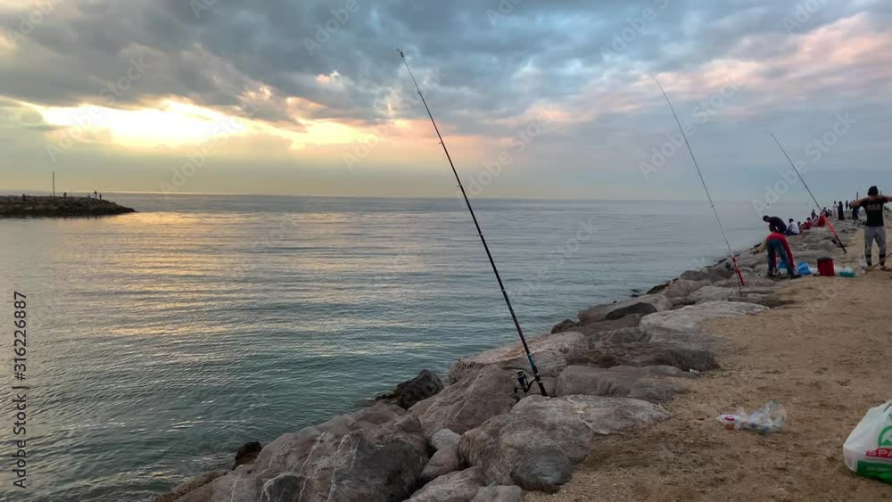 Fishing rod on beach at sunset , many people fishing at the beach using fishing rods Fishing rod on beach at sunset , many people fishing at the beach using fishing rods