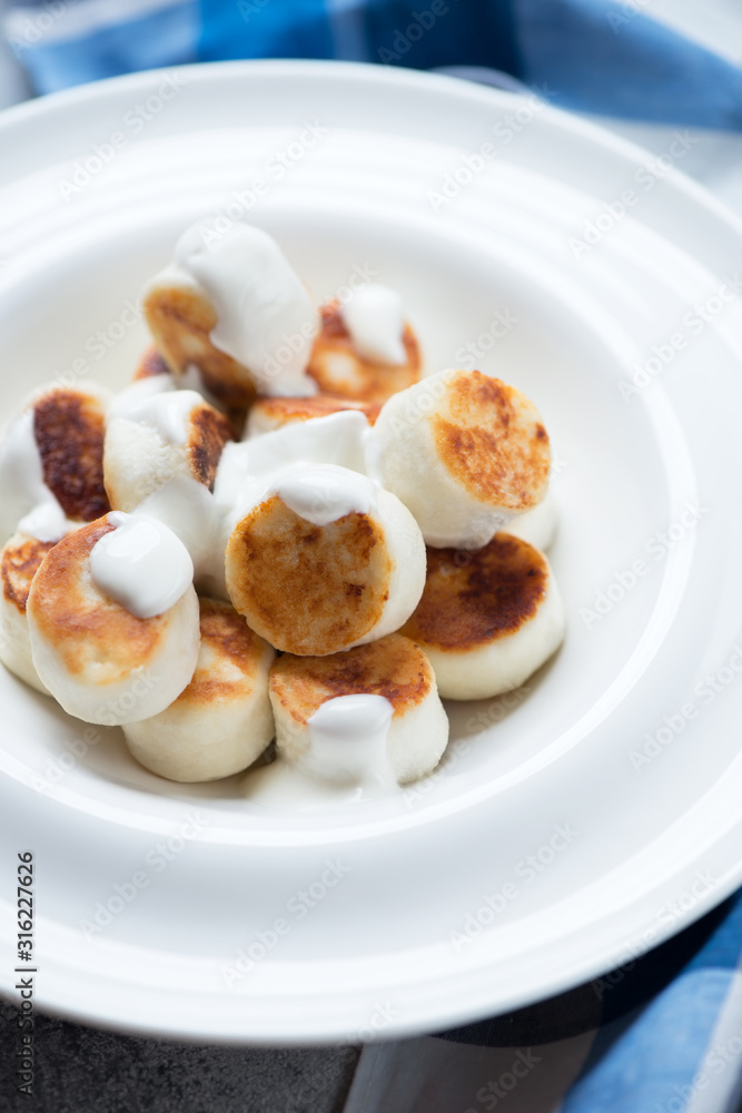 Close-up of fried vareniki or curd dumplings served with sour cream, selective focus, vertical shot Close-up of fried vareniki or curd dumplings served with sour cream, selective focus, vertical shot
