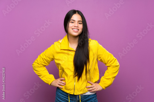 Young teenager Asian girl over isolated purple background posing with arms at hip and smiling © luismolinero