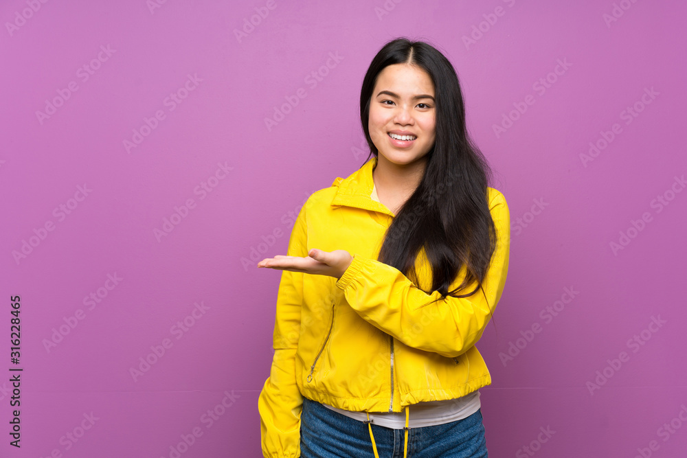 Young teenager Asian girl over isolated purple background presenting an idea while looking smiling towards Young teenager Asian girl over isolated purple background presenting an idea while looking smiling towards