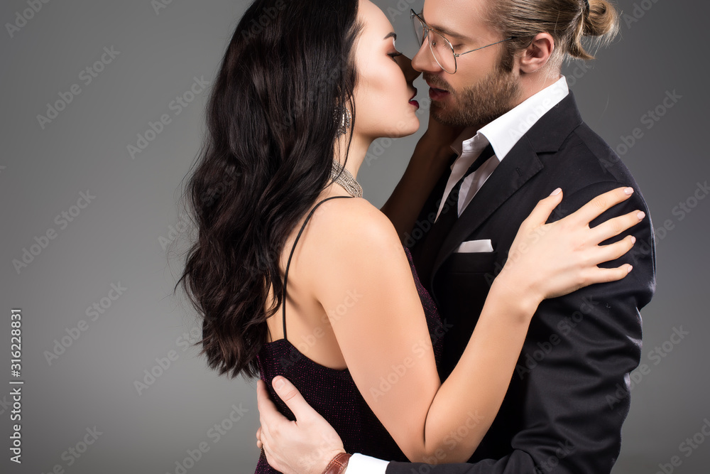 beautiful sensual couple in black suit and dress kissing isolated on grey beautiful sensual couple in black suit and dress kissing isolated on grey