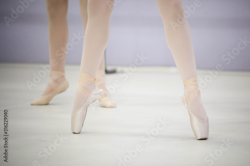  legs of a ballerina in white tights and beige pointes at a training session in the gym