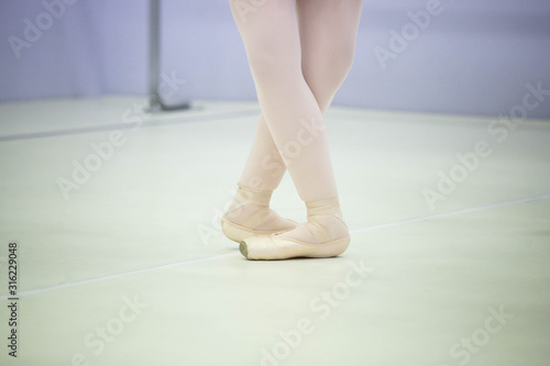  legs of a ballerina in white tights and beige pointes at a training session in the gym