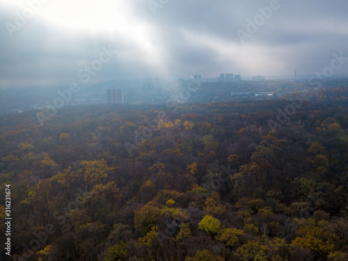 The rays of the setting sun break through the clouds and fall into the autumn forest. Aerial drone view.