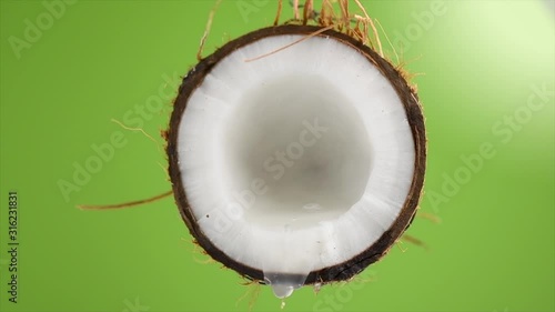 Coconut pouring water, dripping coconut milk, drops of coco nuts oil over green background. Tropical Coco nut closeup. Healthy Food, skin care concept. Vegan food. 4K UHD video, slow motion photo