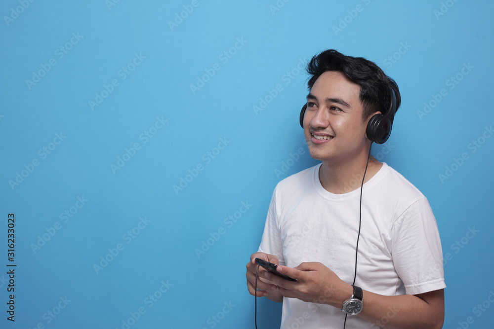 Fototapeta premium Young Asian man listening to music on his smart phone