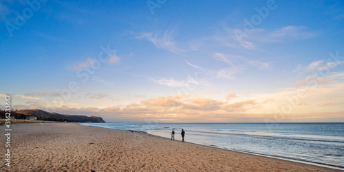 Leute gehen am Meer spazieren, mit Wolken am Horizont und blauem Himmel