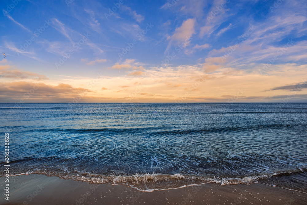 kleine Wellen am Strand mit Wolken in Abendstimmung am Horizont und türkisem Wasser im Meer, Ozean
