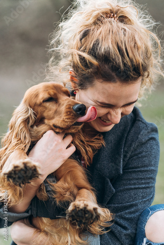 Portrait of cute cocker spaniel on hands of attractive happy smiling young curly woman. Love between dog and humanб