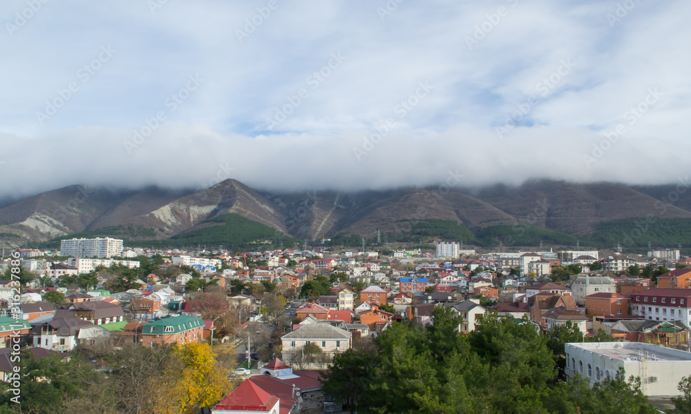 Fototapeta premium City and behind mountains with peaks in the clouds. Summer