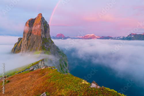 Pink dawn with a rainbow above the clouds in Norway on the mountain Segla