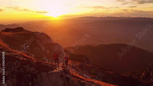 Aerial 4k drone clip with couple of hikers watching a beautiful sunset on top of Bucegi mountain ridge, during magical golden hour light in autumn season, in Romania