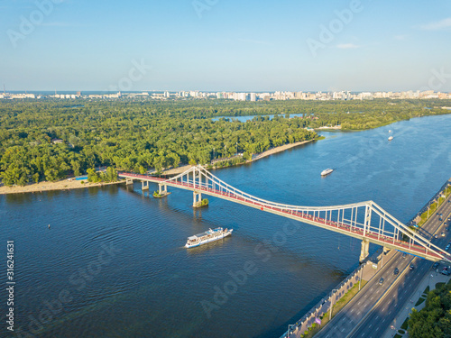 Aeiral drone view. The boat floats under a pedestrian bridge along the Dnieper River in Kiev.