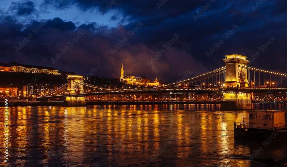 Night View Of Szechenyi Bridge. Famous Chain Bridge Of Budapest. Beautiful lighting and reflection in the Danube River.