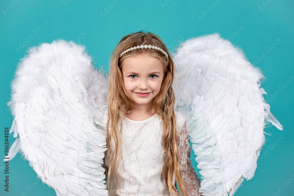 Cute child girl in white dress standing over color background. Beautiful little angel. Cute toddler girl in white wings as Cupid. Valentines day.